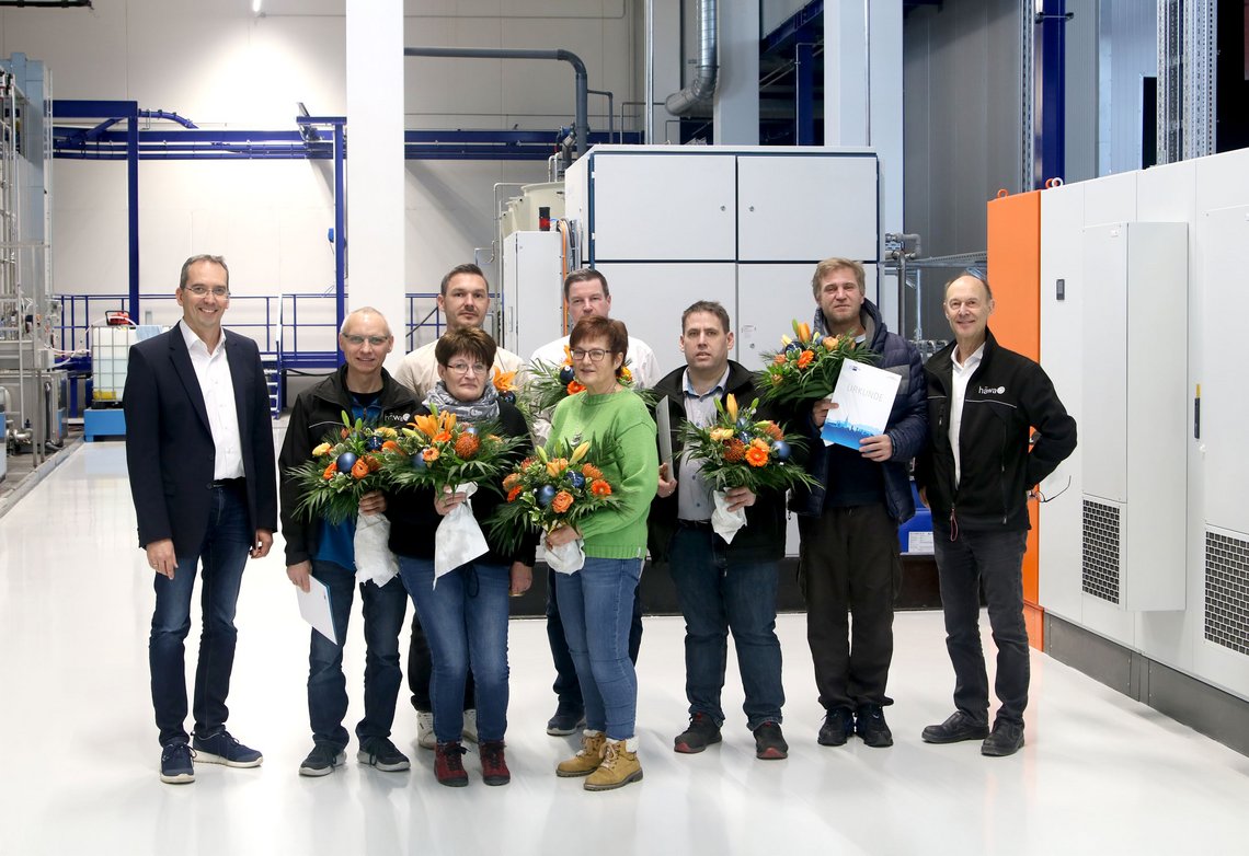 Gruppenfoto von Jubiläums-Mitarbeitern. Manche von ihnen halten einen Blumenstrauß in den Armen.